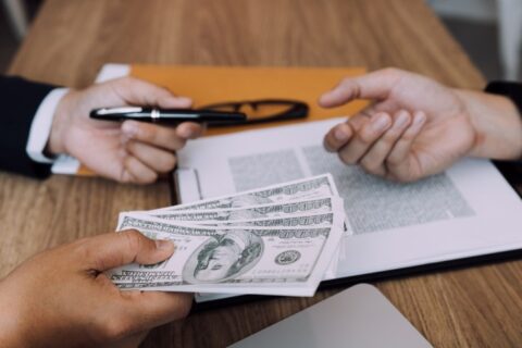 Two people at a table in the DFW Metroplex hold money and a pen, discussing responsible loan use