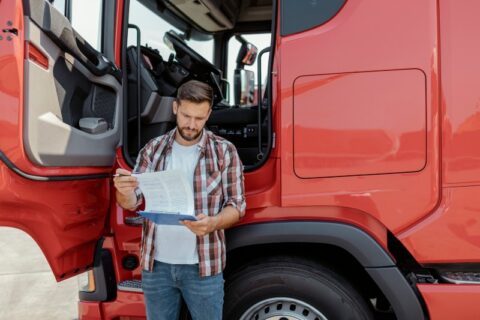 A man holding paperwork for a Title Loan on his red Commercial Semi Truck in the DFW Metroplex